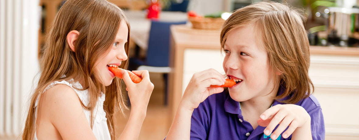 KI generiert: Zwei Kinder essen gemeinsam rote Paprikastücke in einer Küche.