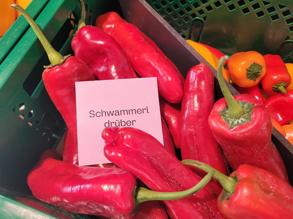 KI generiert: Kiste mit roten Paprikaschoten; Text: "Schwammerl drüber".